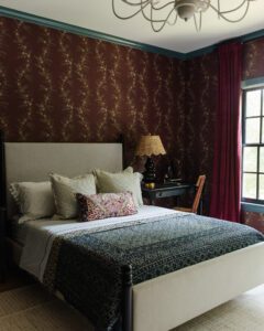 Beautifully decorated bedroom featuring a plush bed, patterned bedding, and vintage-style wallpaper. Natural light streams through the window, highlighting the warm, inviting atmosphere.