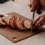 Hands slicing a seasoned turkey breast on a cutting board