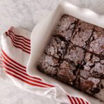 A white dish of peppermint brownies next to a red & white tea towel