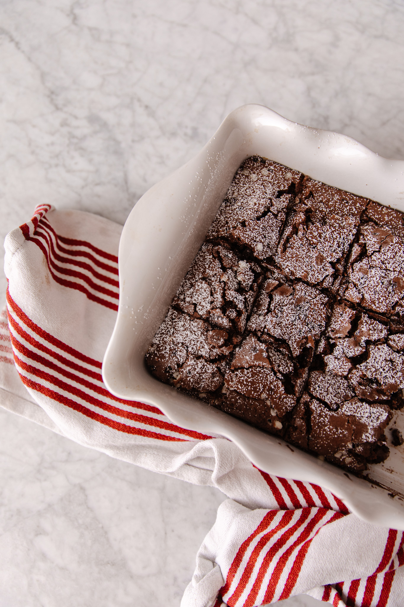 A white dish of peppermint brownies next to a red & white tea towel