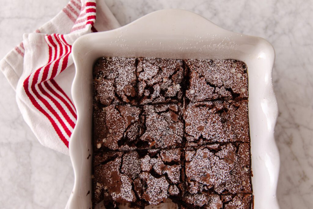 A white baking dish filled with chocolate brownies topped with powdered sugar