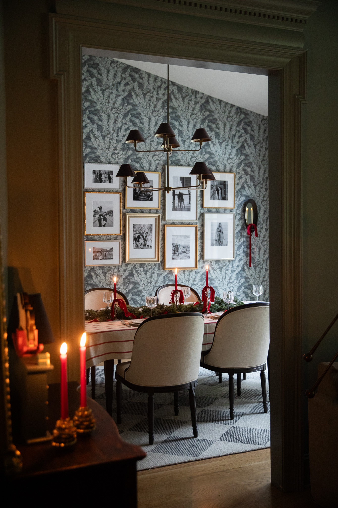 An inviting look into a dining room set for Christmas with red taper candles, red ribbon, and a cream and red stripe tablecloth