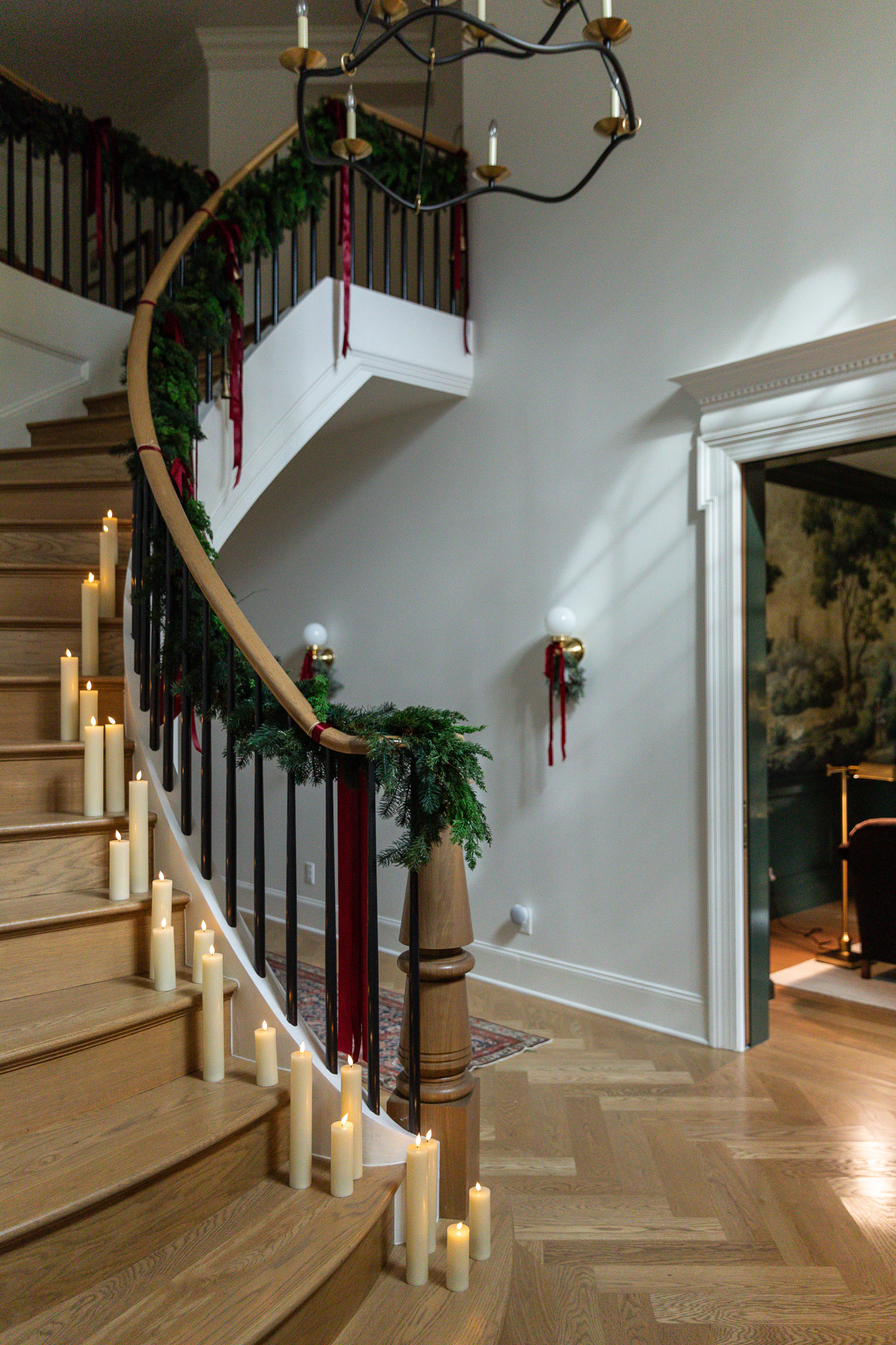 A grand staircase at Christmas with stairs lined with battery candles and a green garland down the handrail with burgundy bows