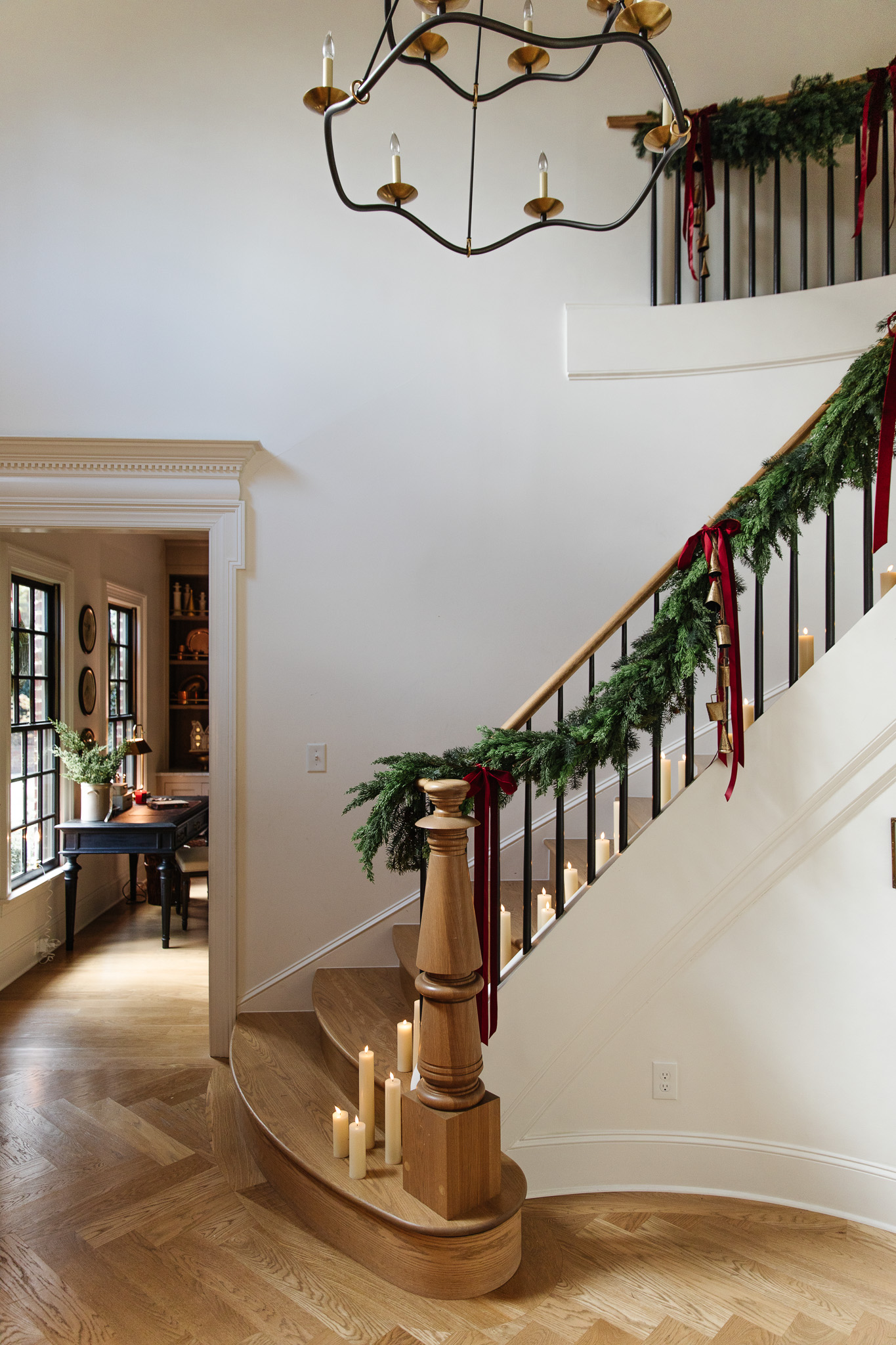 A grand staircase at Christmas with a green garland down the handrail and burgundy bows