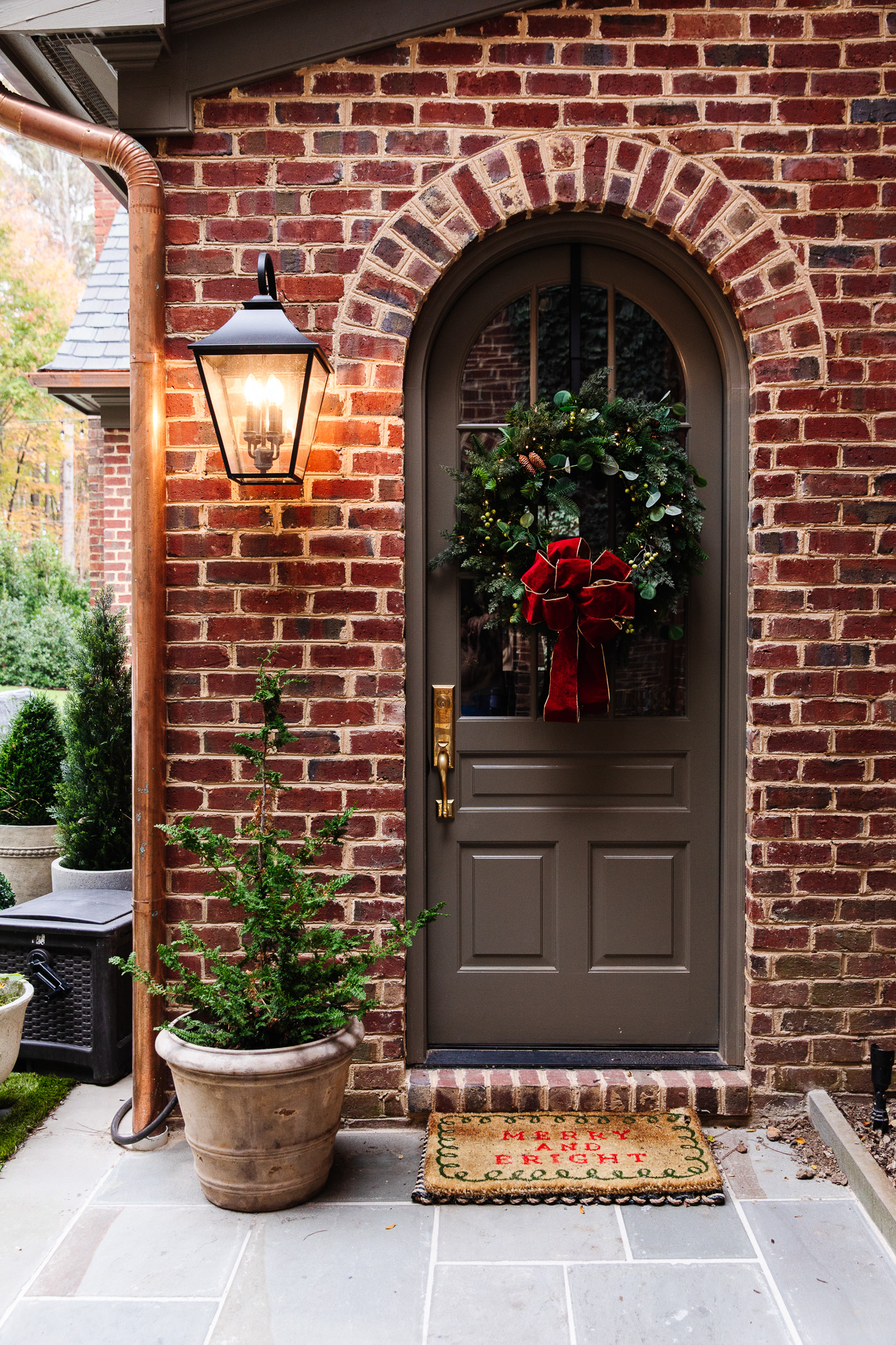 A curved brown door and a traditional green wreath with a gold-lined red bow