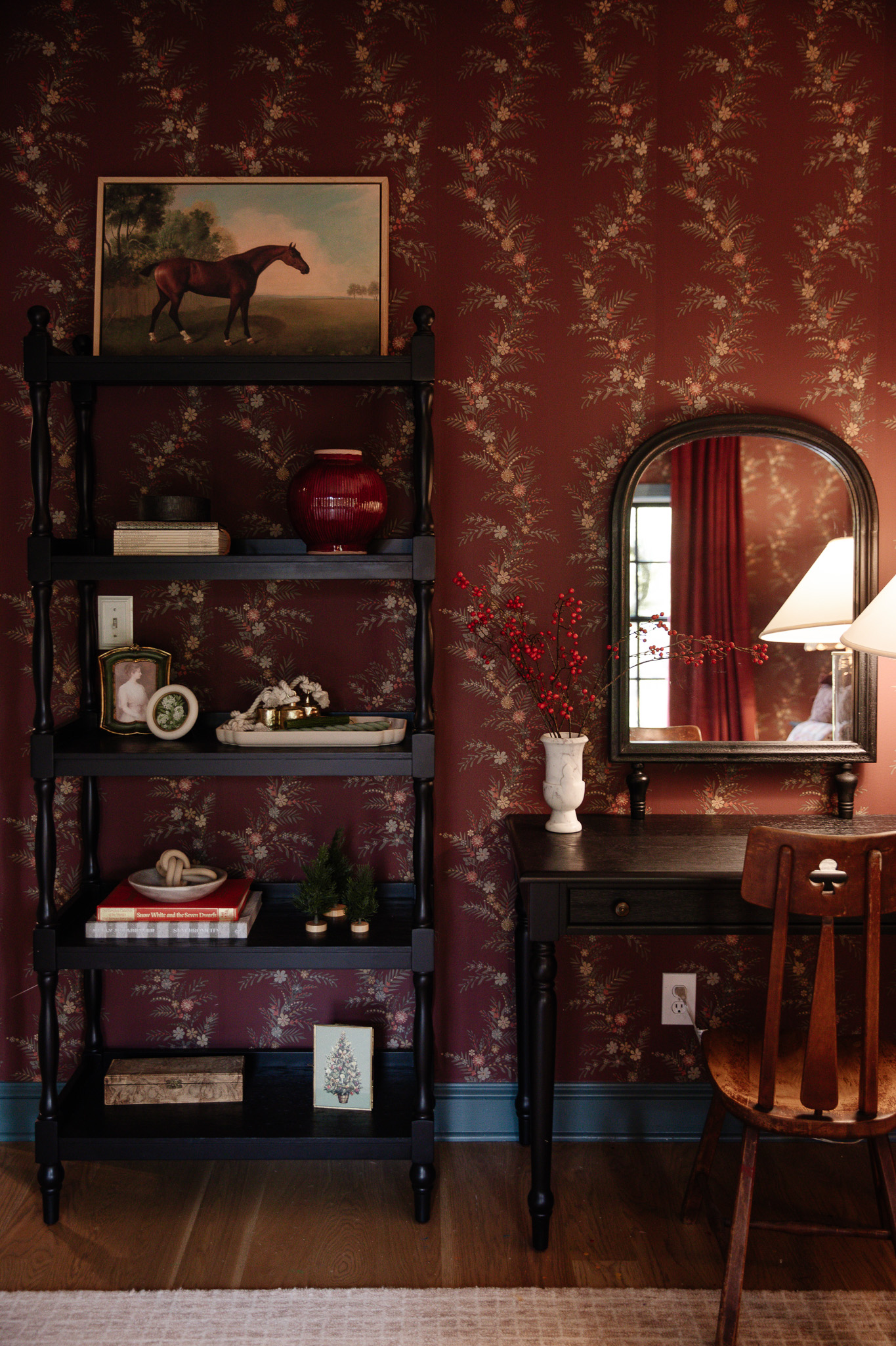 A girl's desk and open bookcase decorated with red berry stems in a white marble vase and other red decor accents