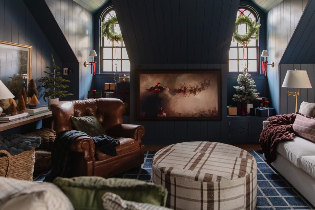 A Christmas scene in a cozy living area with wreaths in the windows, small evergreen trees in nooks, and a vintage Santa and reindeer screensaver on the Frame TV