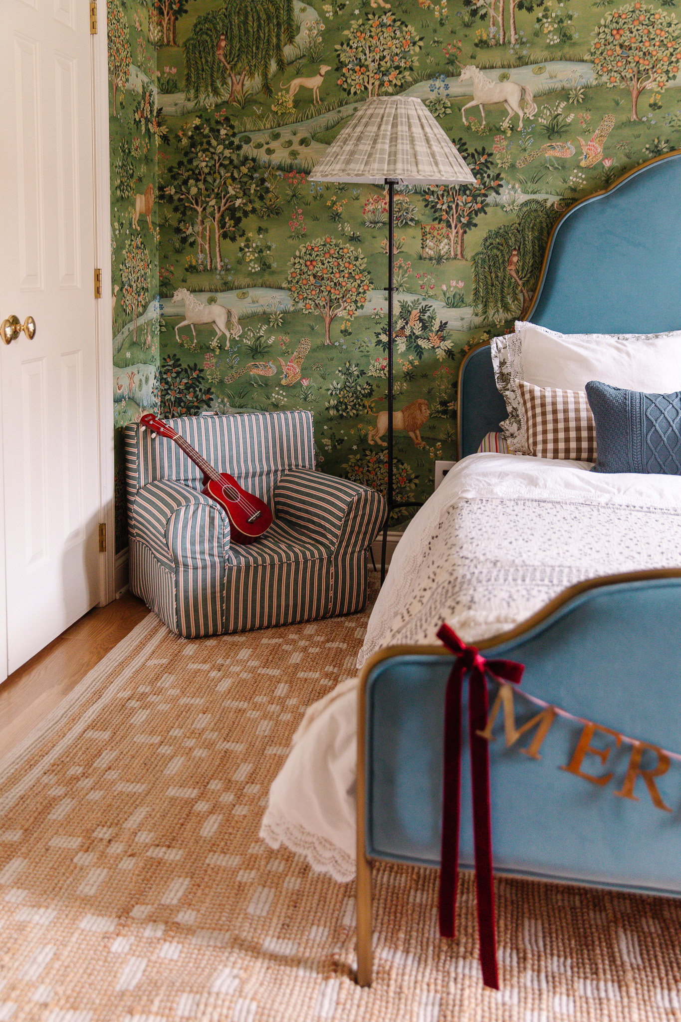 A child's Pottery Barn chair with a small guitar on it and a Merry Christmas garland hanging across the footboard of an upholstered blue bed