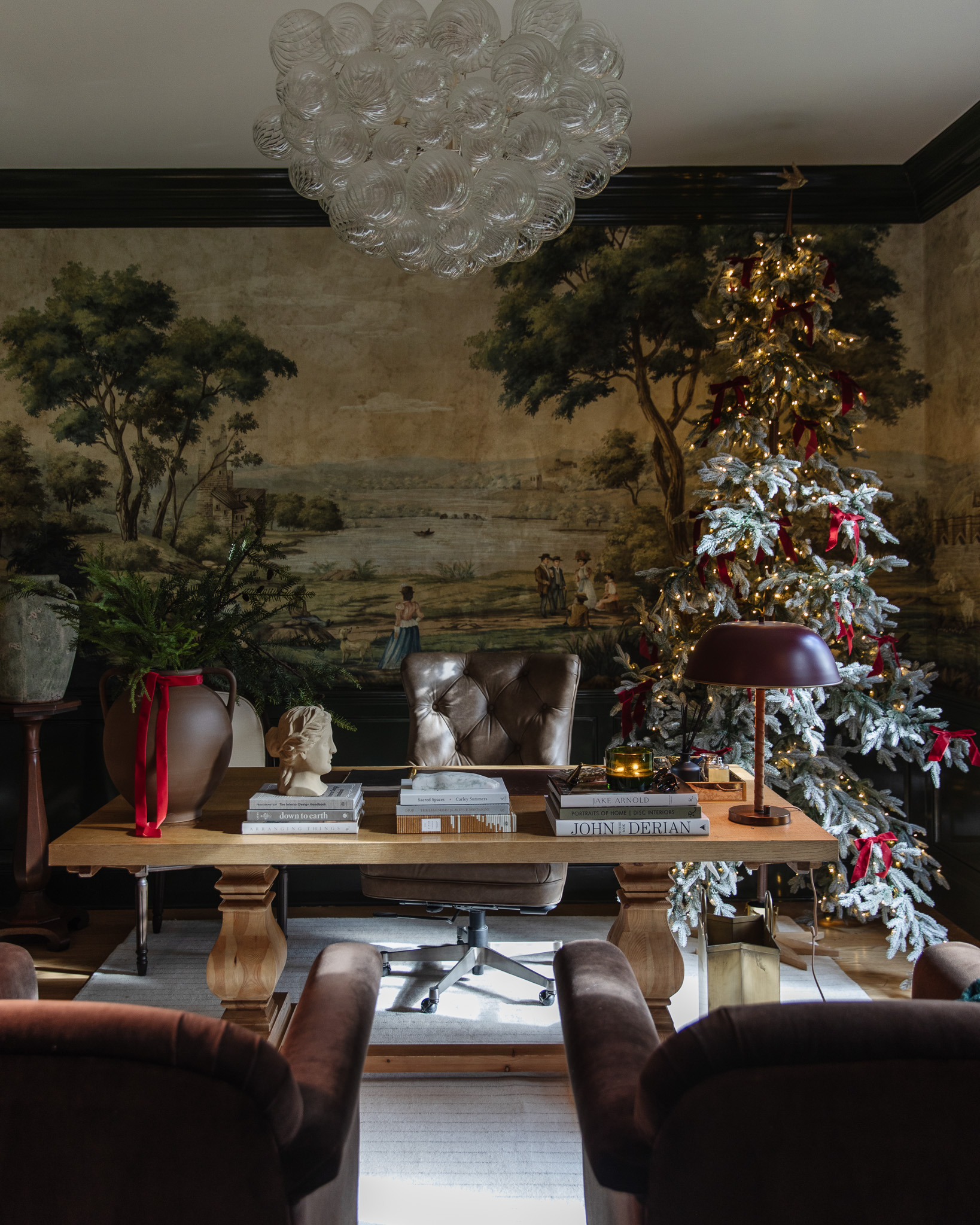 The study with a lit Christmas tree and bright-red bow accents tastefully placed throughout the room.