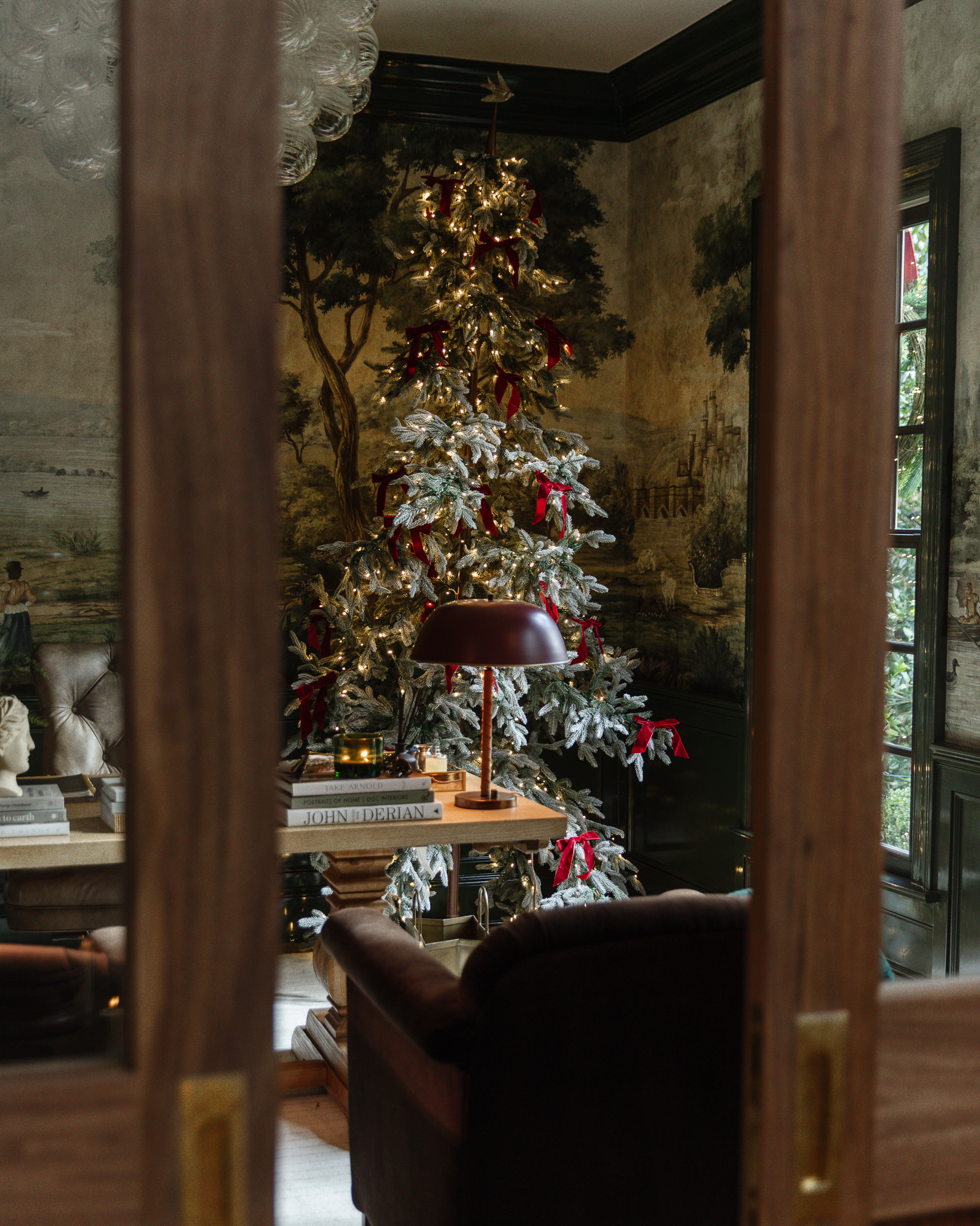 A flocked Christmas tree with red ribbons in a study behind a desk