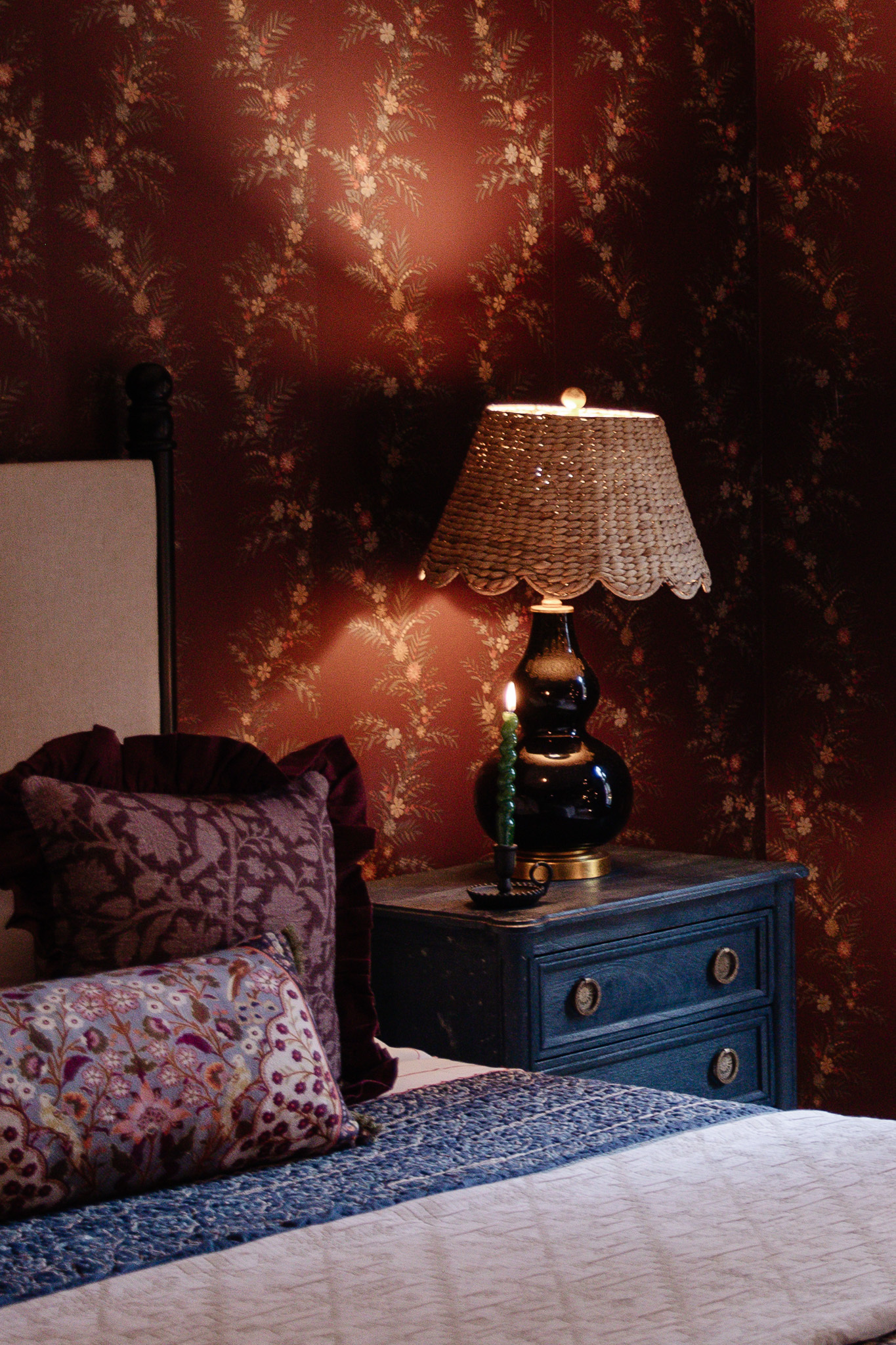 A green swirling candle in a brass candlestick holder on a nightstand