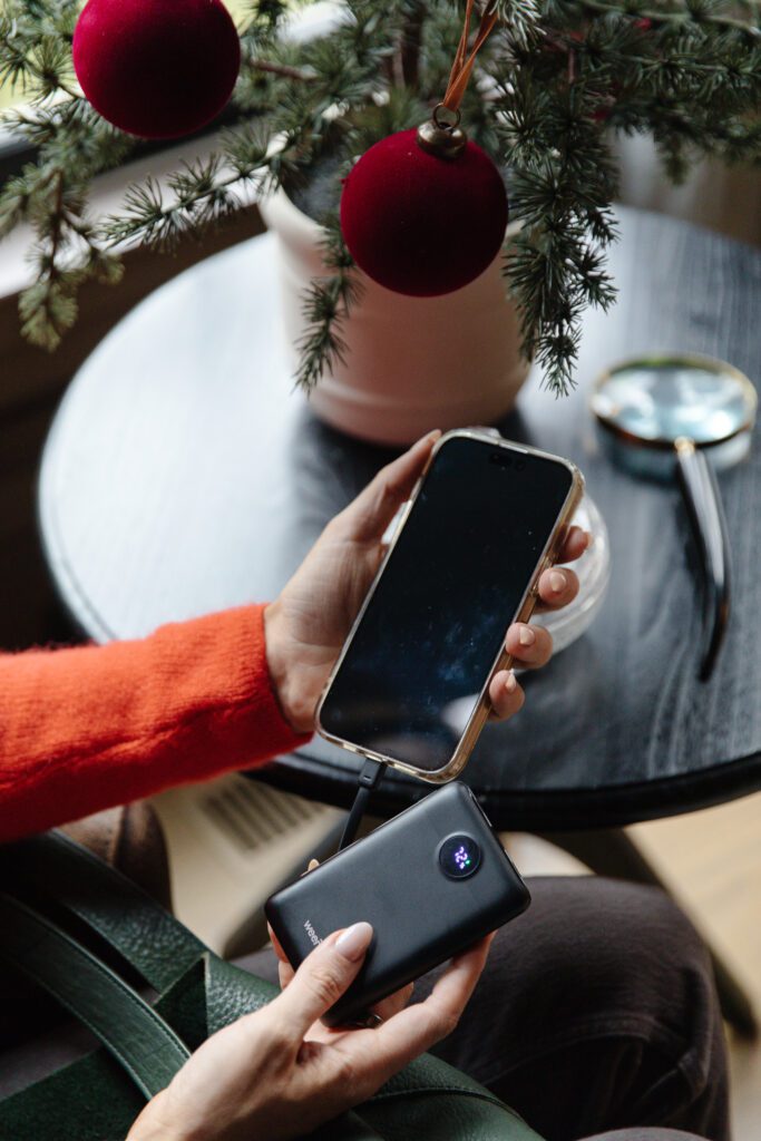 A hand holding an iPhone next to a portable power bank phone charger