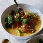A soup spoon drizzling sweet & spicy chili oil into a Singapore Noodles-inspired Chicken Noodle Soup