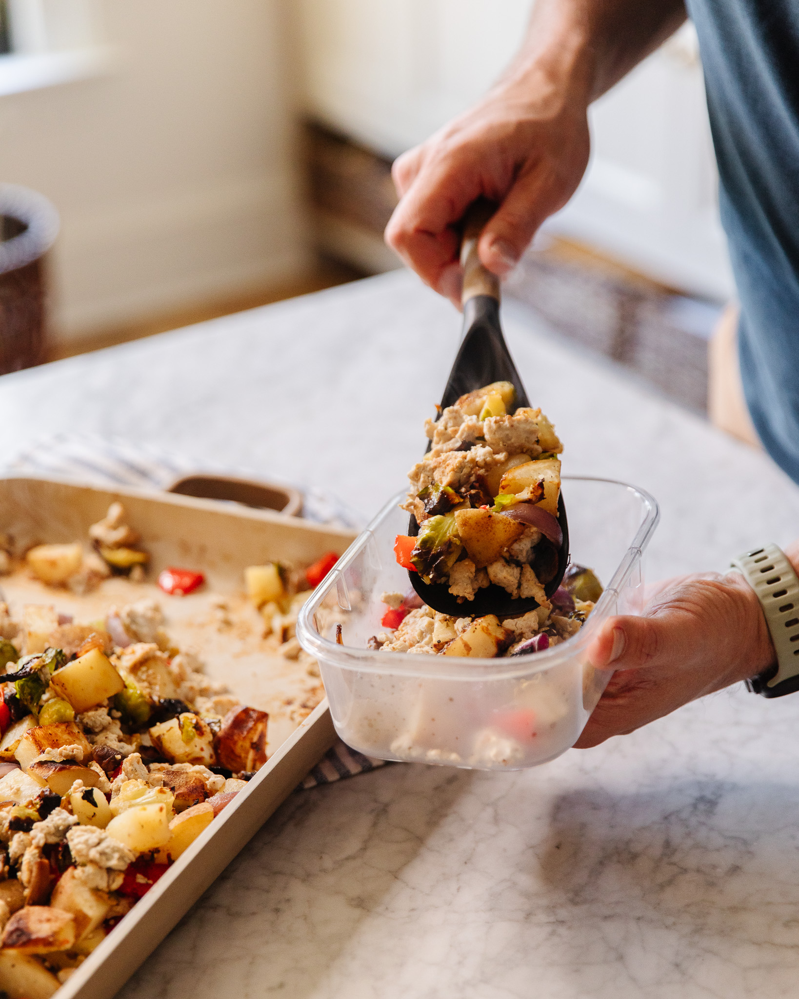 Hand scooping a portion of breakfast hash into a container for meal prep