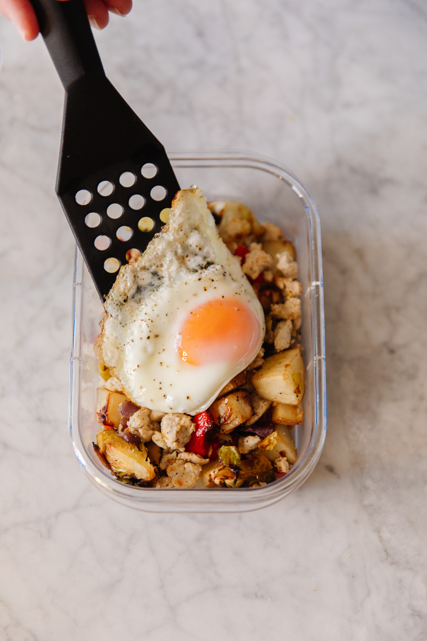 Spatula placing an over-easy egg over a portioned-out breakfast hash