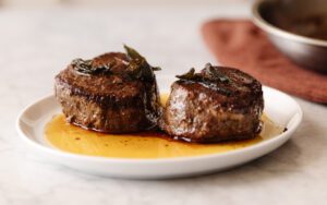 Two seared filet mignon steaks on a serving plate with crispy sage on top