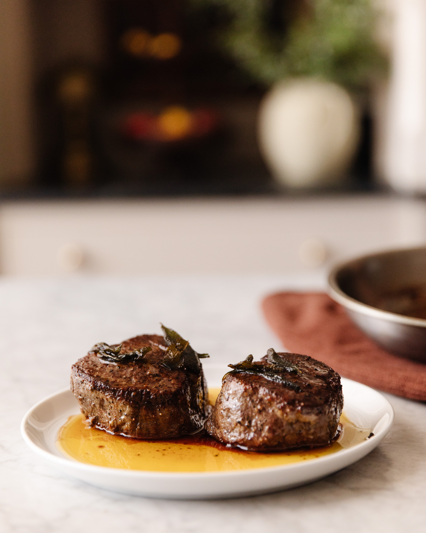 Two seared filet mignon steaks on a serving plate with crispy sage on top