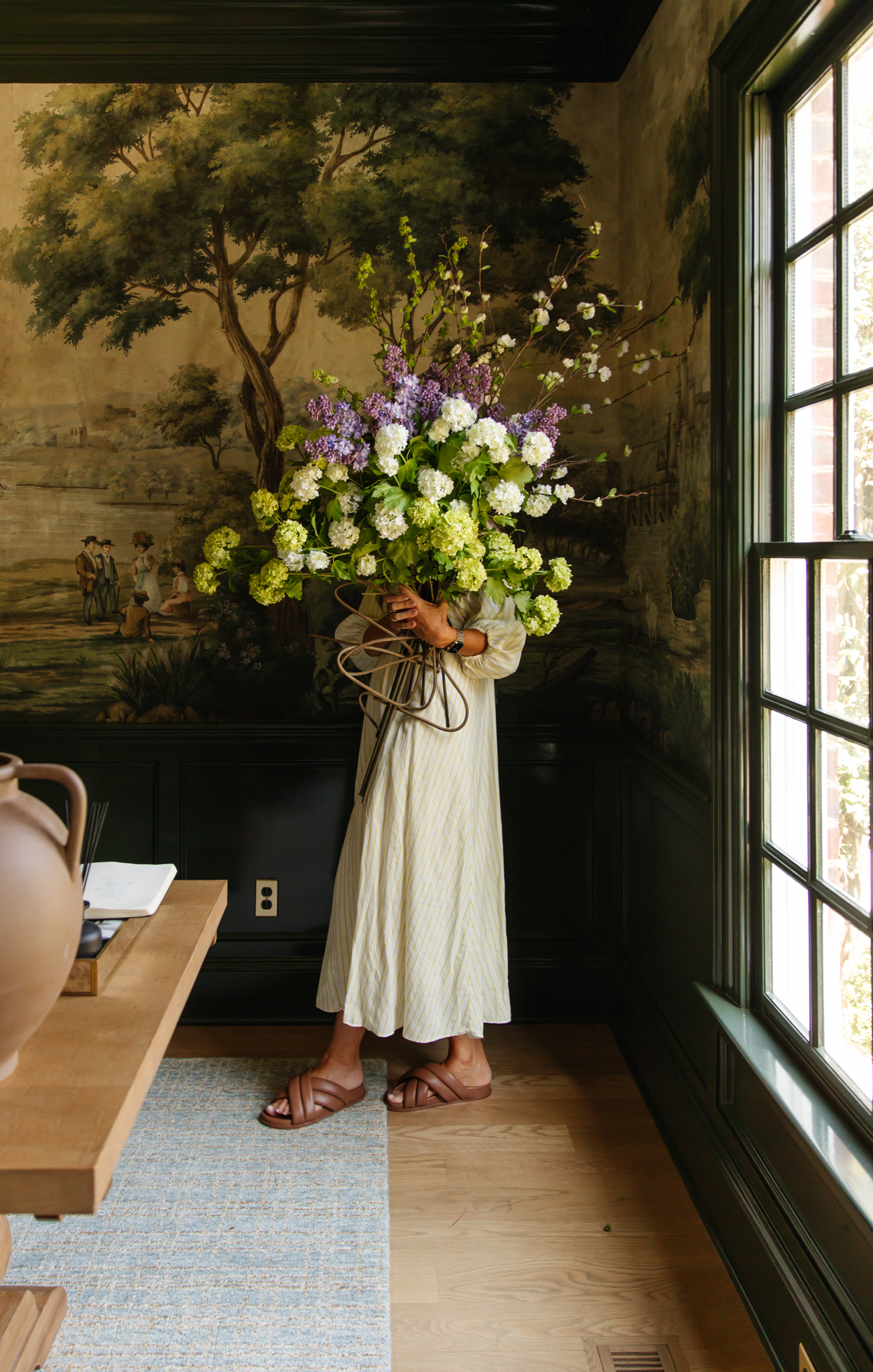 Julia in a white dress holding a large bouquet of green and white faux floral stems