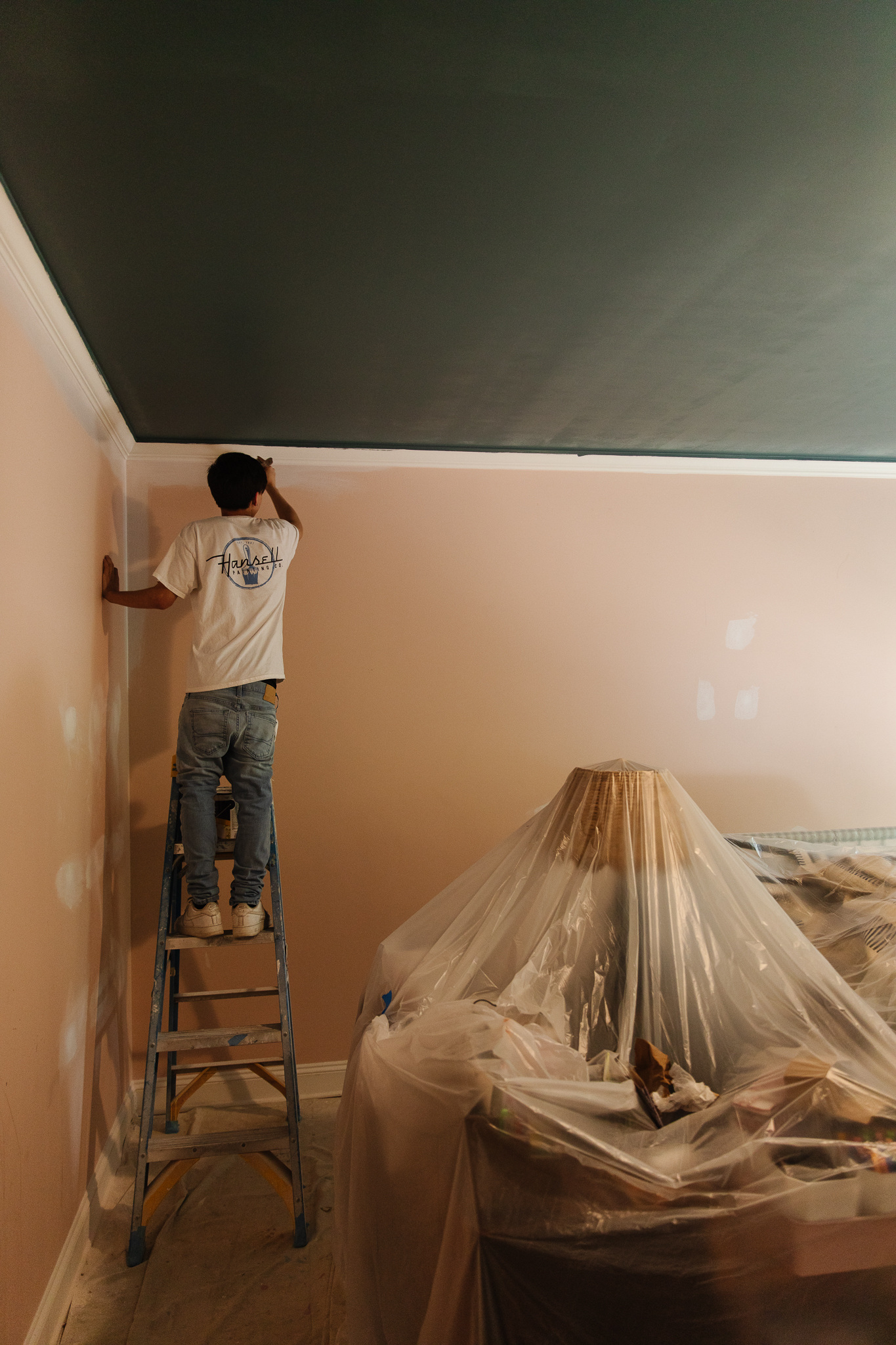 A painter adding dark blue ceiling to Greta's room. 