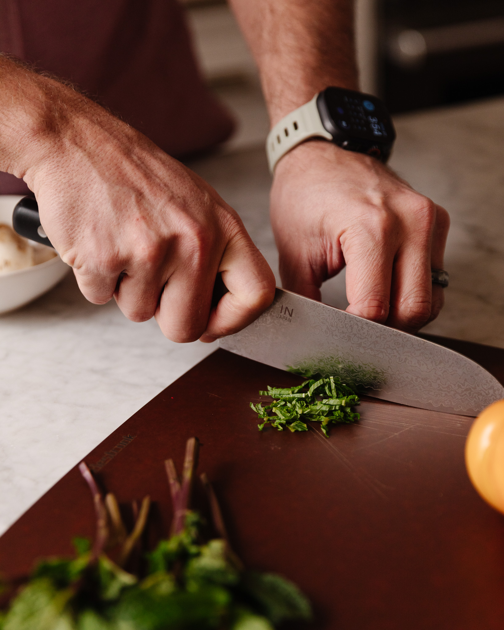 Hands slicing some herbs on a dark cutting board