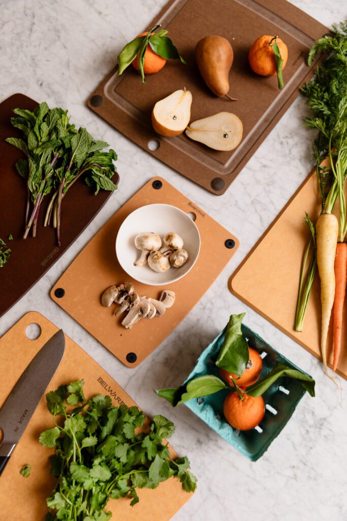 5 cutting boards in a grid on a marble countertop with various fruits, herbs and vegetables