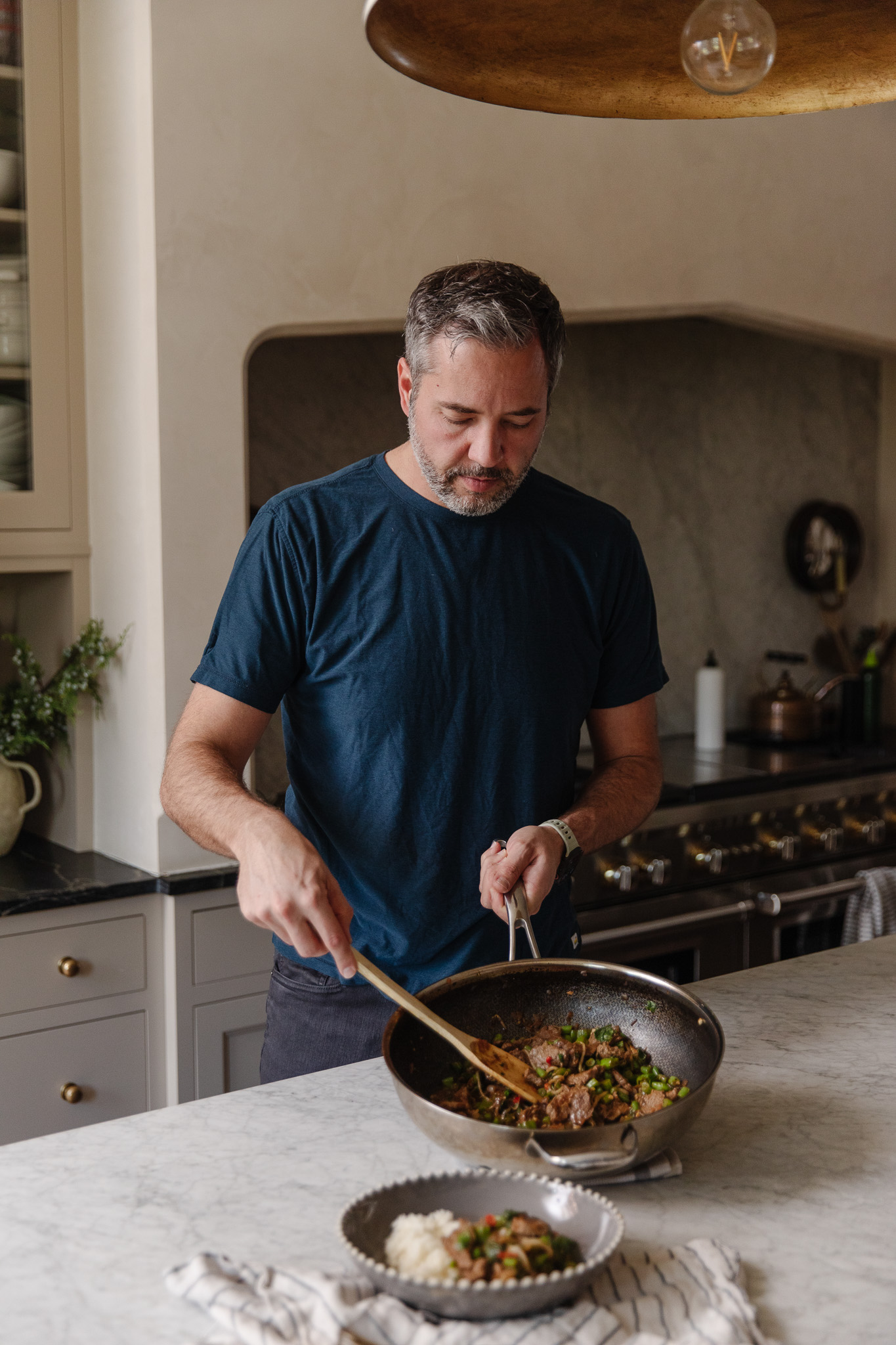 Chris dishing out basil beef stir-fry from a wok to a bowl