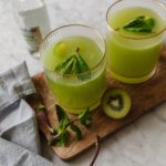 Two glasses of kiwi cucumber spritzer next to some cut kiwi and mint leaves