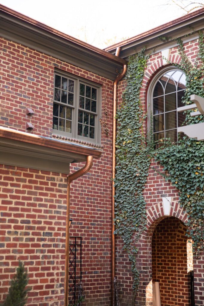 Side view of brick home with copper gutters next to ivy walls