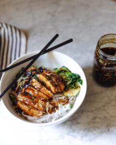 DIY teriyaki sauce next to a bowl of teriyaki chicken and rice noodles
