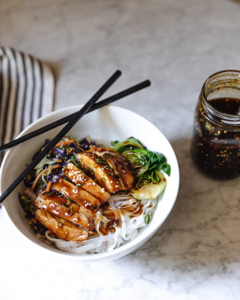 DIY teriyaki sauce next to a bowl of teriyaki chicken and rice noodles