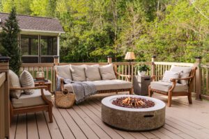A cozy outdoor sitting area with sofa and two side chairs around a fire table on a deck
