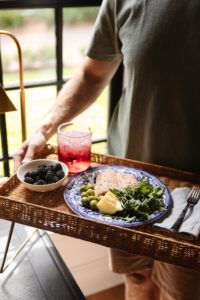 Chris holding a rattan tray with a plate of food, bowl of fruit, and pretty drink on it
