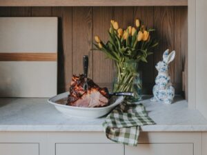 Easter ham next to yellow tulips and blue & white ceramic bunny