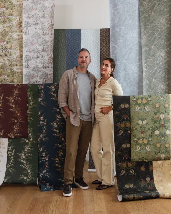 Chris and Julia standing in front of a display of various wallpaper samples, showcasing their home decor style and interior design expertise.