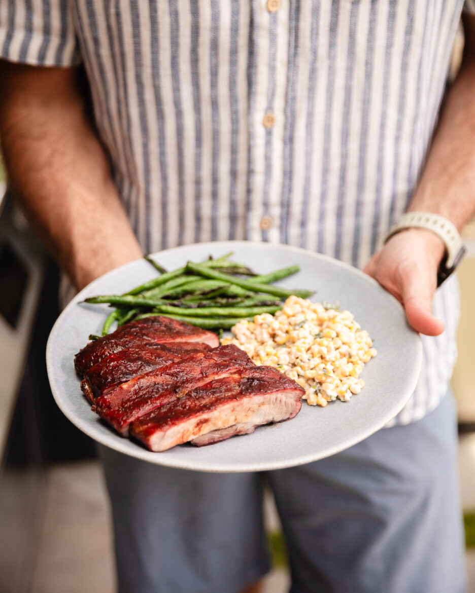 Chris holding a plate of sliced ribs, corn salad and green beans