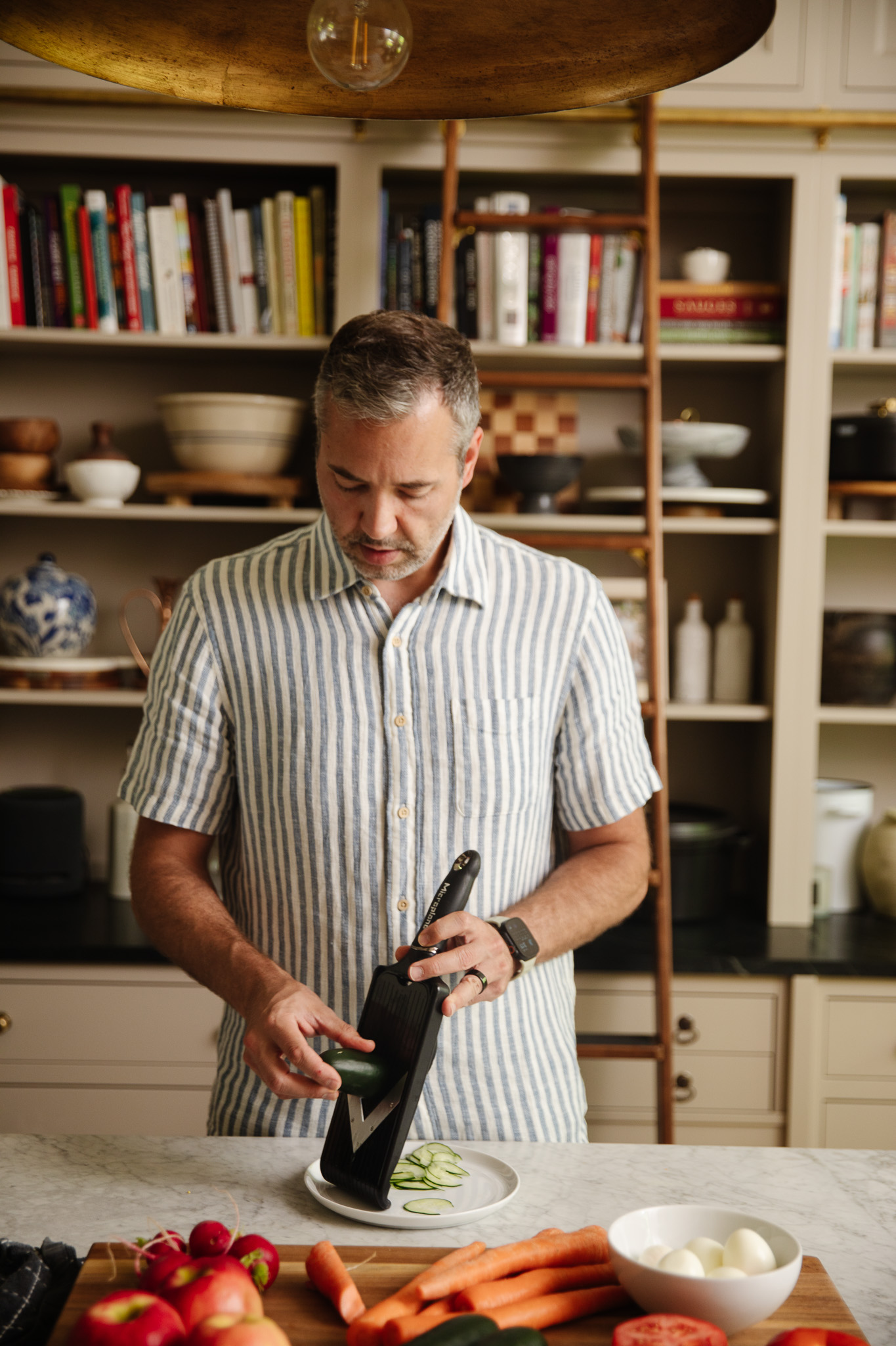 Chris using a mandoline kitchen tool to slice vegetables and fruit