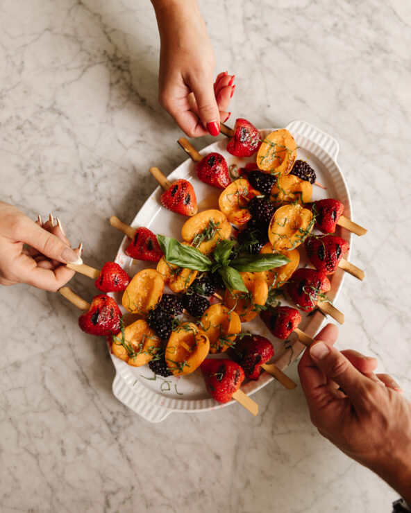 Hands reaching in to take a fruit skewer from a platter