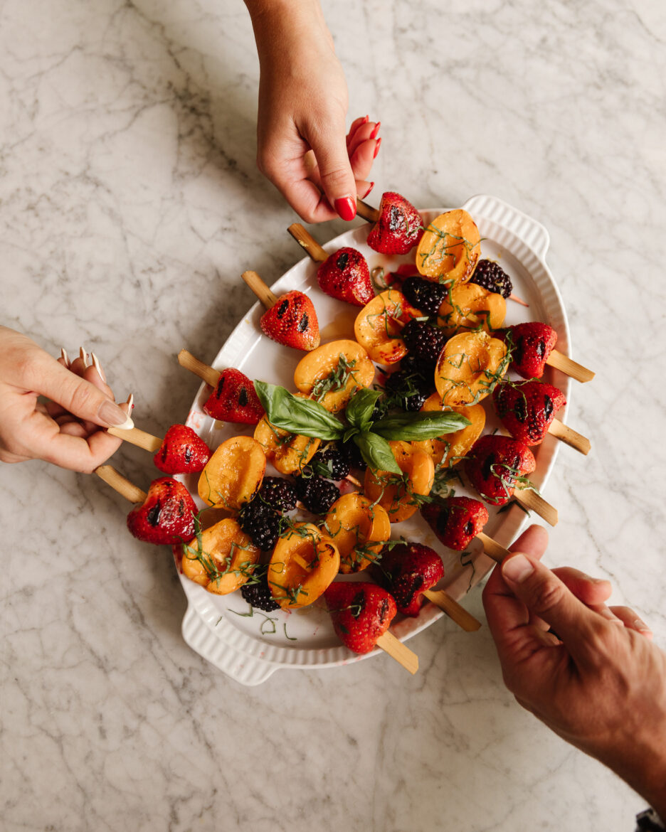 Hands reaching in to take a fruit skewer from a platter