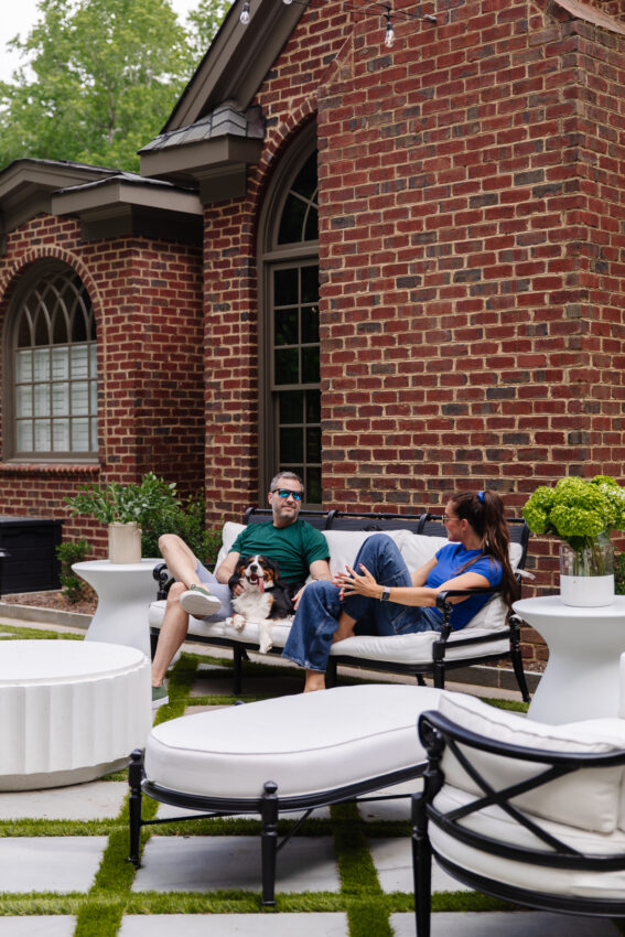 Outdoor sofa with two people and a dog, set against a brick house exterior, showcasing a cozy and stylish outdoor living space perfect for relaxing and entertaining.