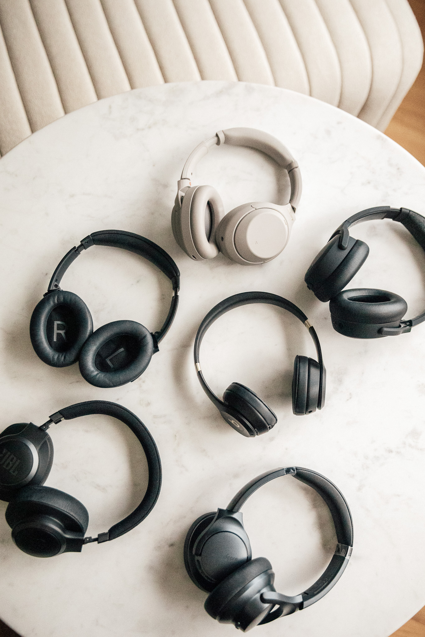 A flat-lay of 7 different over-the-ear headphones on a marble side table