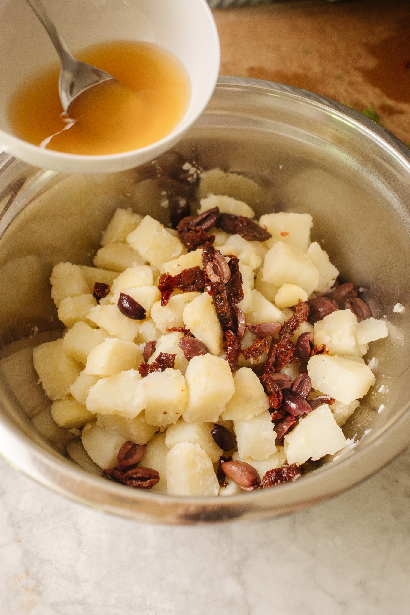 A bowl of freshly boiled cubed russet potatoes with a dressing about to spooned overtop