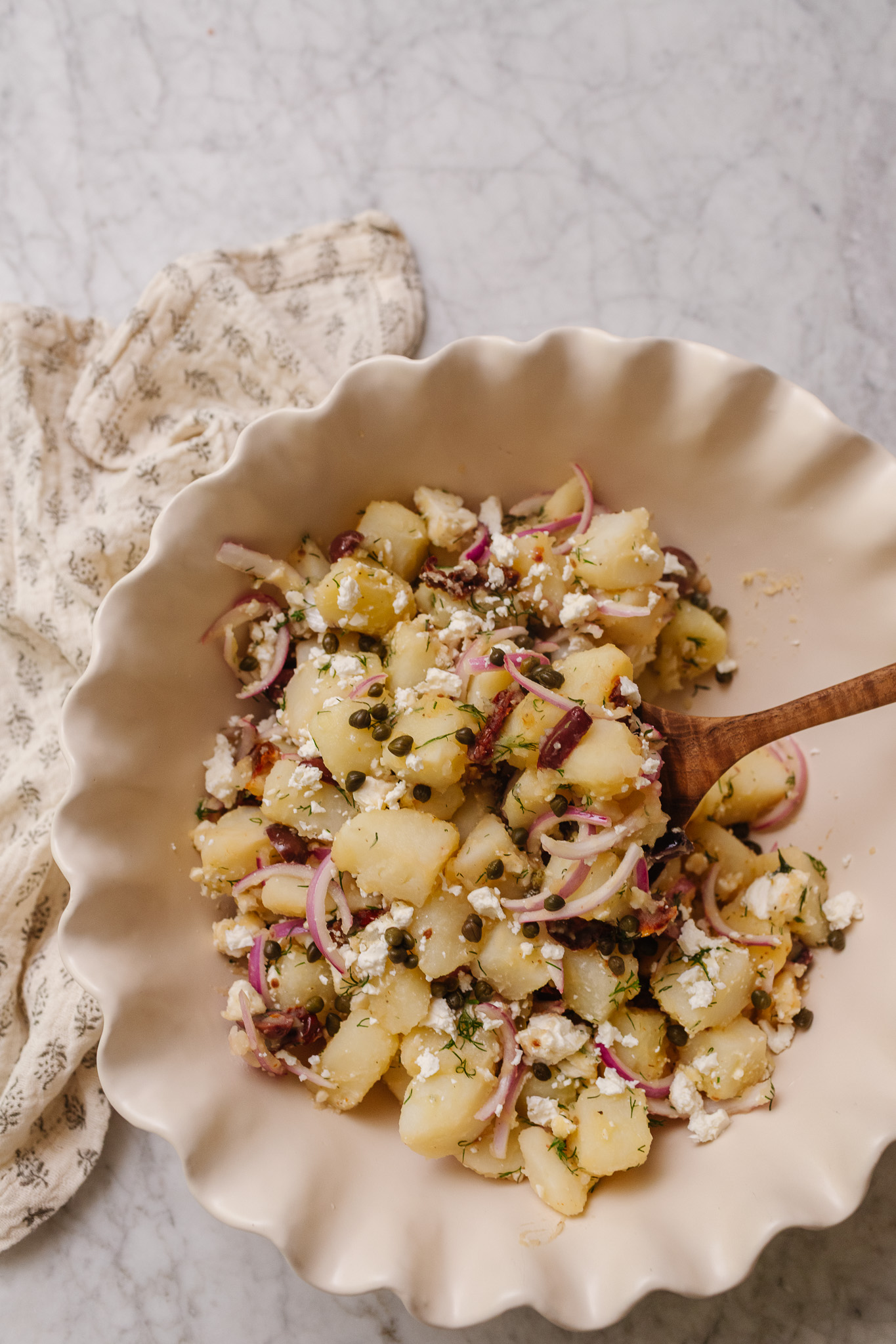 A scalloped bowl filled with a Greek Potato Salad