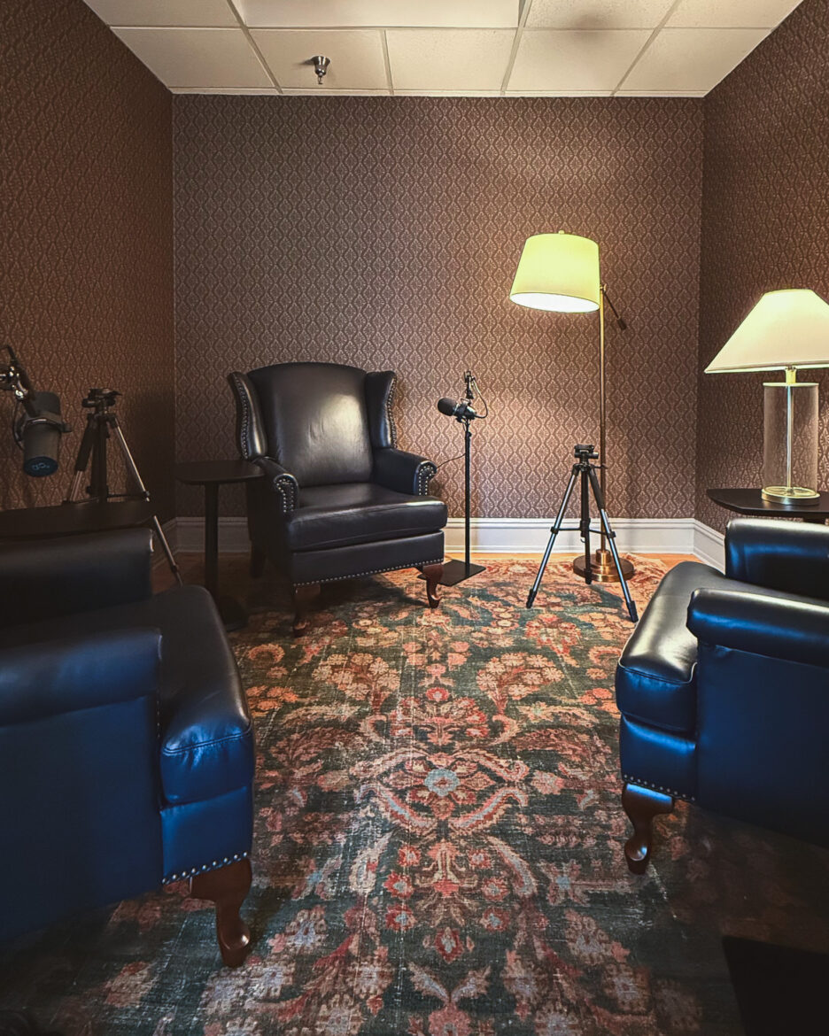 A room with three wingback chairs, maroon wallpaper, and a traditional-style rug