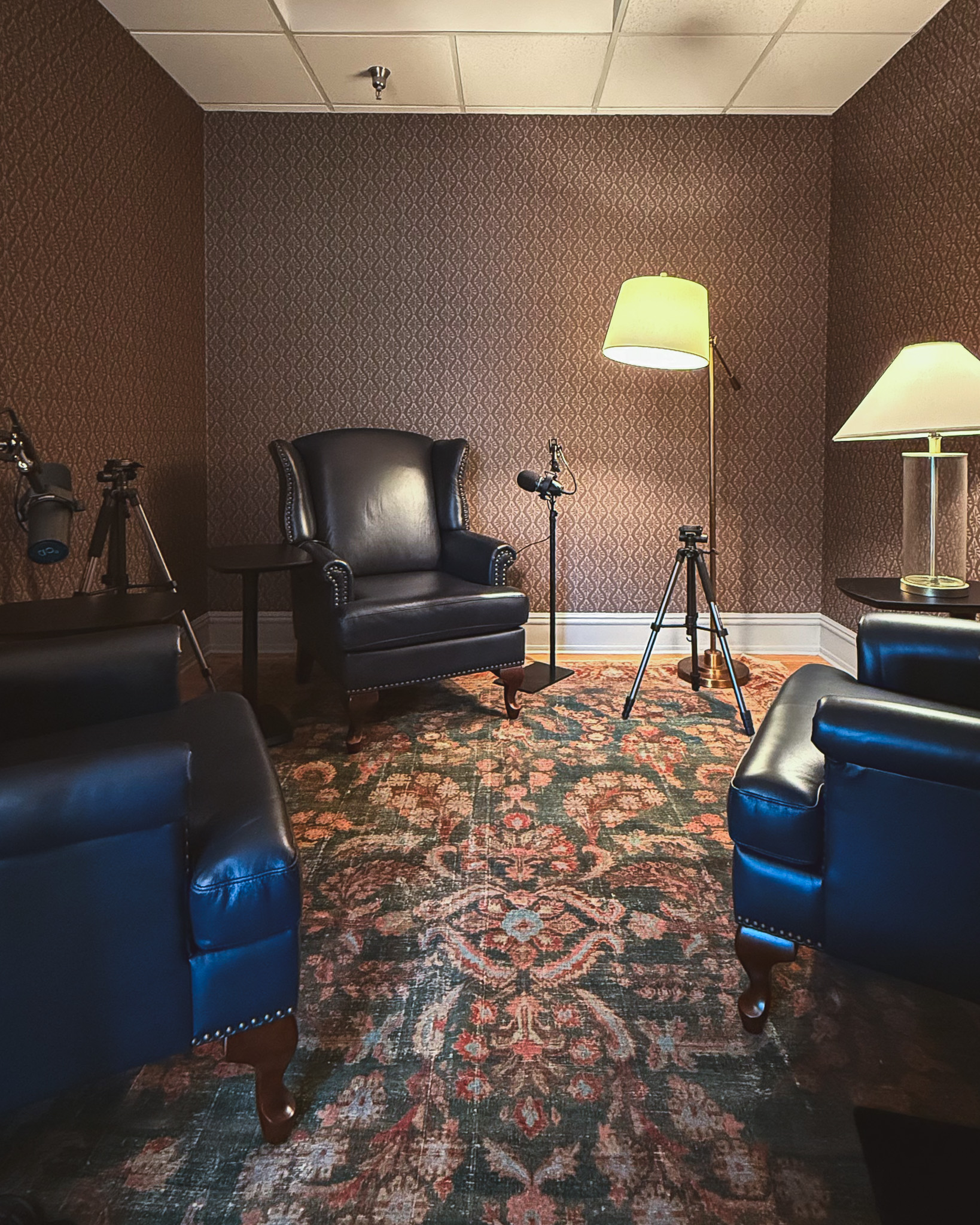 A room with three wingback chairs, maroon wallpaper, and a traditional-style rug