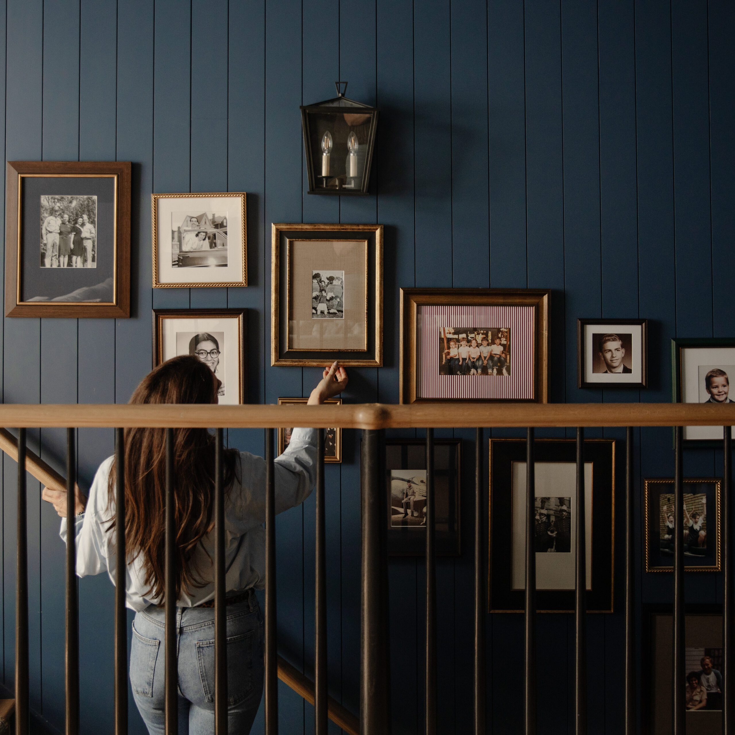 Julia straightening a vintage family photo on a picture wall in a stairway