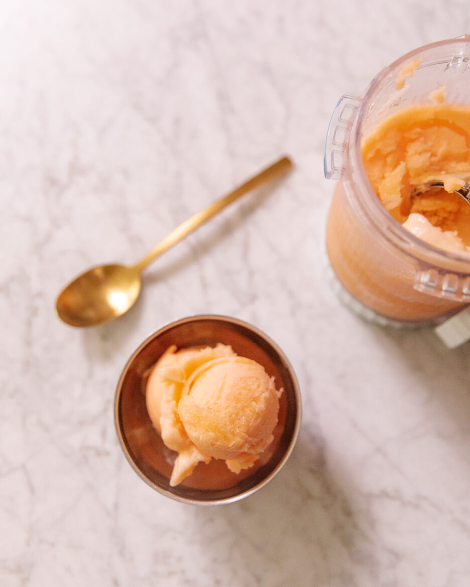 A bowl of cantaloupe sorbet next to the Ninja Creami canister and a spoon