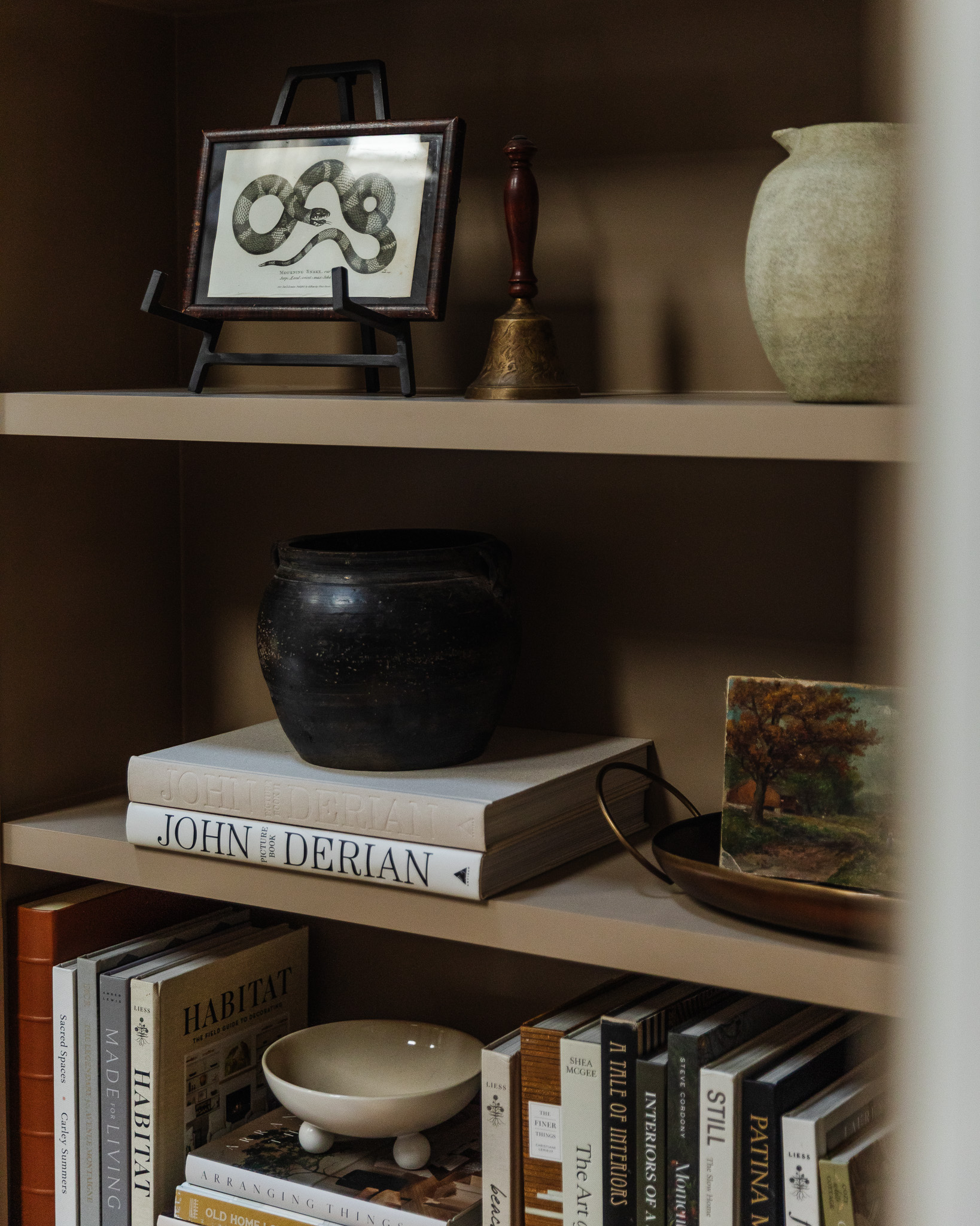 Living room bookshelf with coffee table books, a vase, miniature art on an easel and a vintage bell