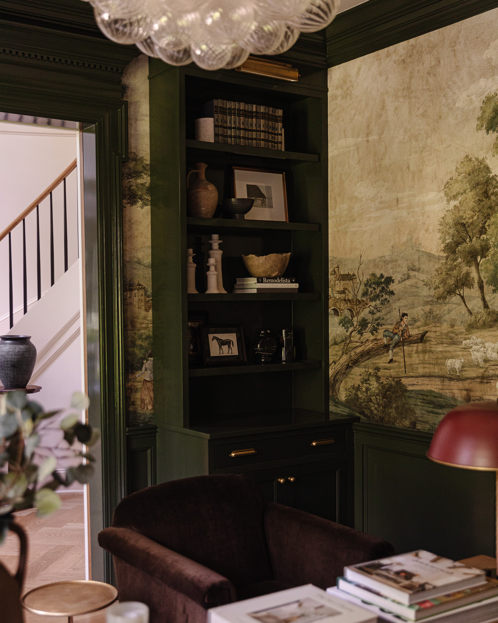 A built-in bookcase painted green styled with vases, art and candlesticks
