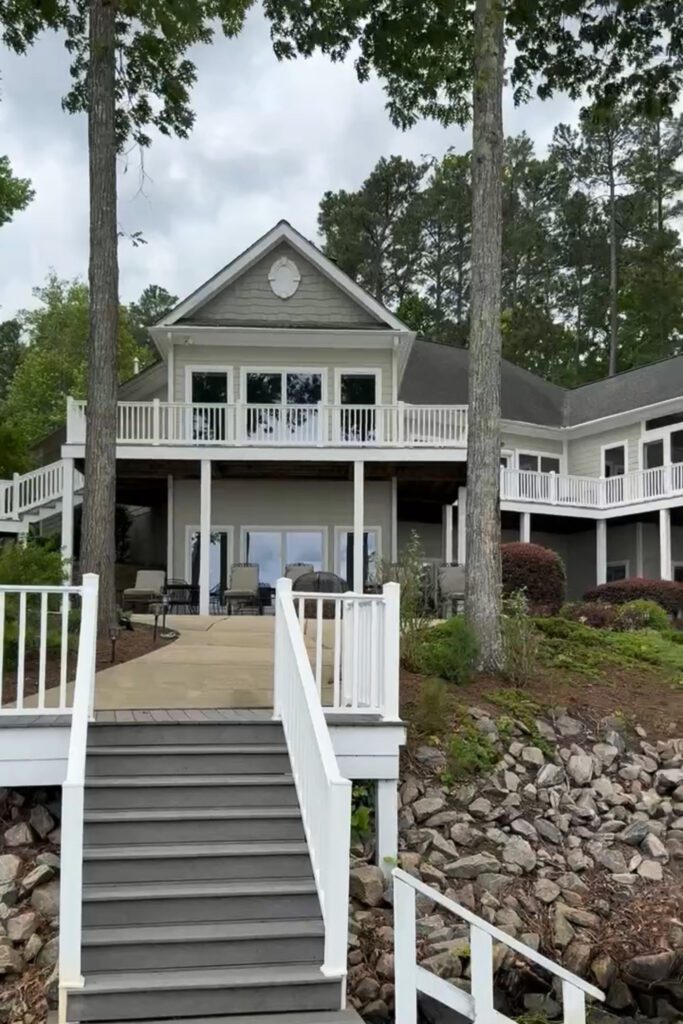 A back view of the lake house with a wraparound 2nd-level porch and stairs down to the lake