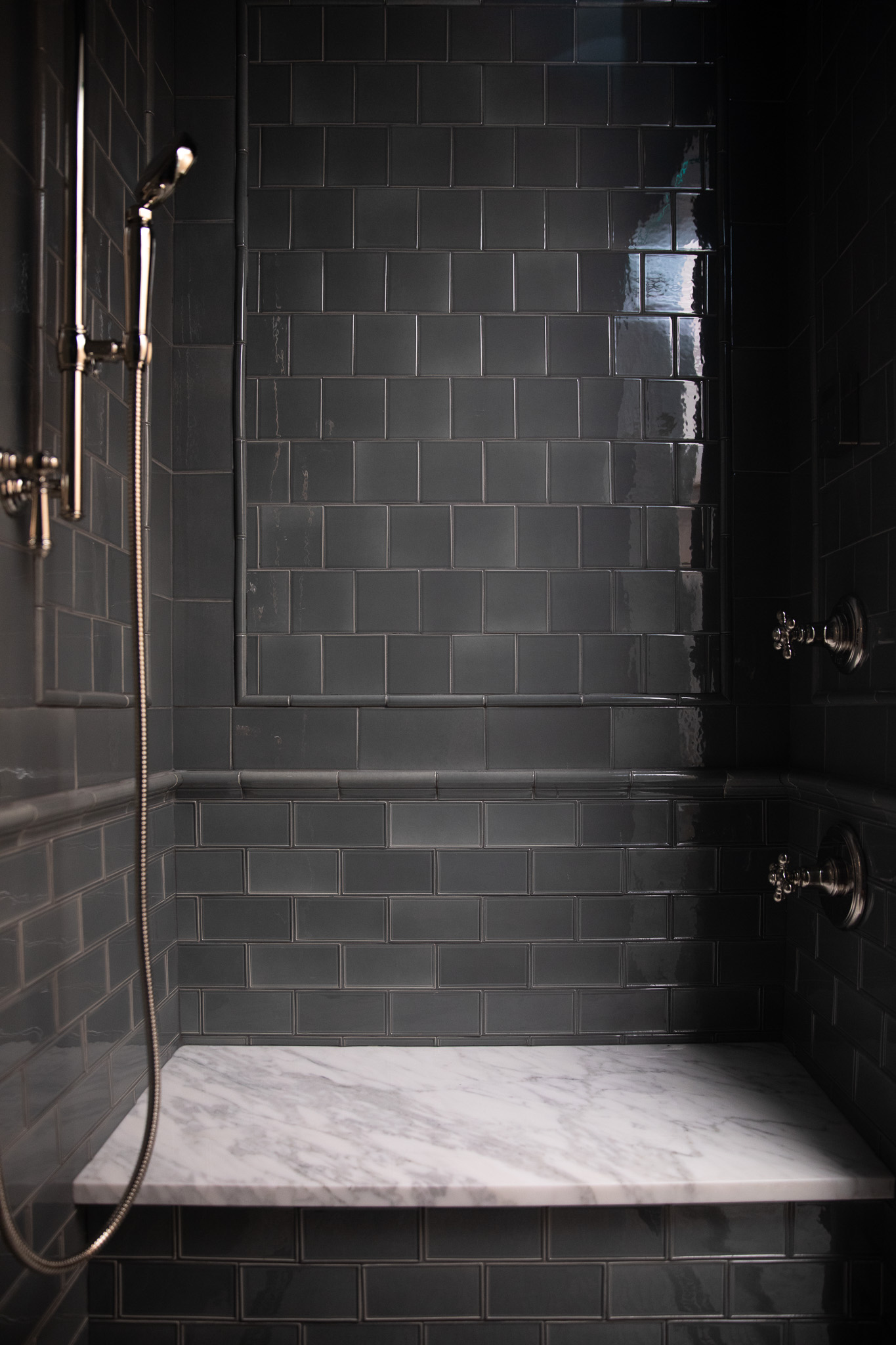 Elephant Ear earthenware tile by Ann Sacks in a primary bathroom shower with polished nickel Kohler fixtures. A marble shower seat in white and gray sits atop the gray-green tile.